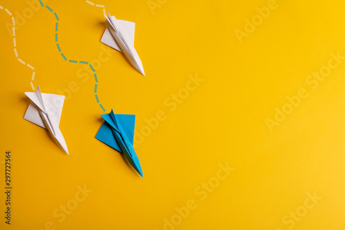 Group of paper plane in one direction and with one individual pointing in the different way on yellow background. Dotted line from aircraft tail.