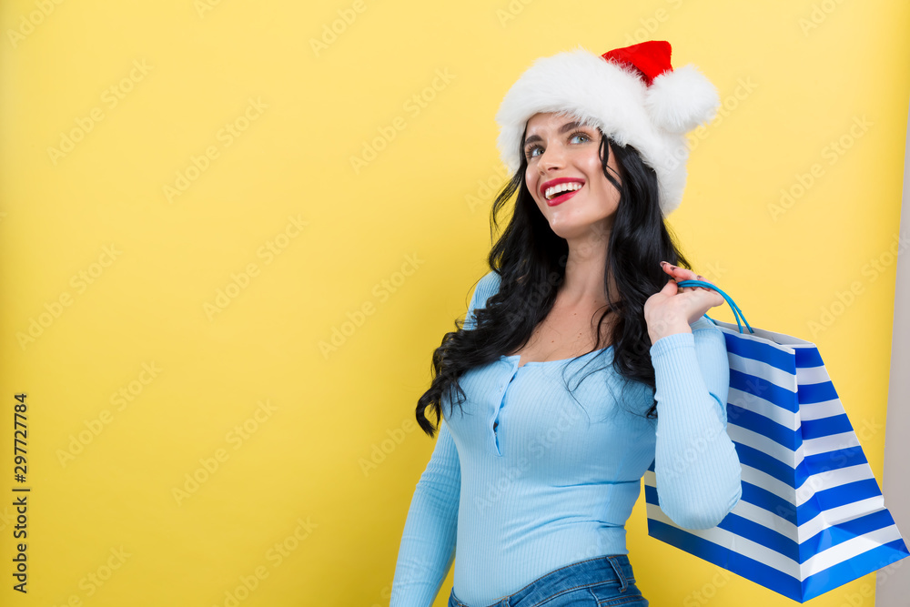 Young woman with santa hat holding a shopping bag on a yellow background