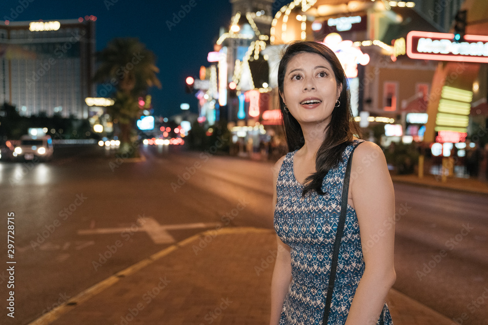 Beautiful girl traveler in dress on background of night city with many billboard lights shinny in bokeh view. curious woman tourist smiling looking around on urban street in las vegas nevada summer