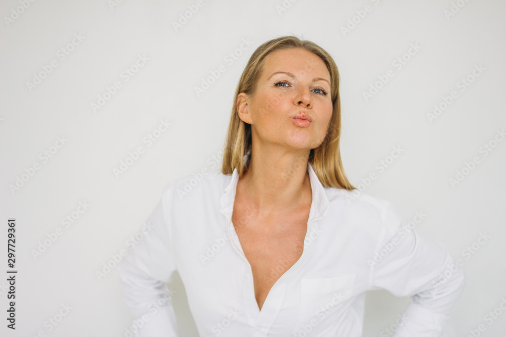 Portrait of kissing blonde forty year woman with long hair in shirt on white wall background isolated
