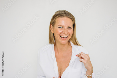 Portrait of happy blonde forty year woman with long hair in white shirt on white wall background isolated