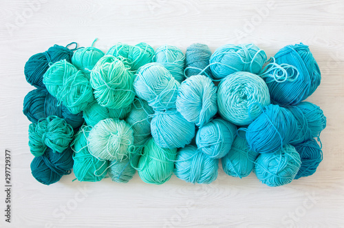 Yarn of green, turquoise, aquamarine and blue colors. White wood background. Knitting needles and crochet hooks. Scissors. White background.