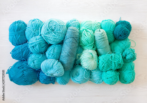 Yarn of green, turquoise, aquamarine and blue colors. White wood background. Knitting needles and crochet hooks. Scissors. White background.