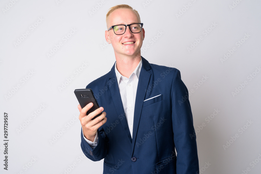 Happy young blonde businessman in suit thinking while using phone Happy young blonde businessman in suit thinking while using phone