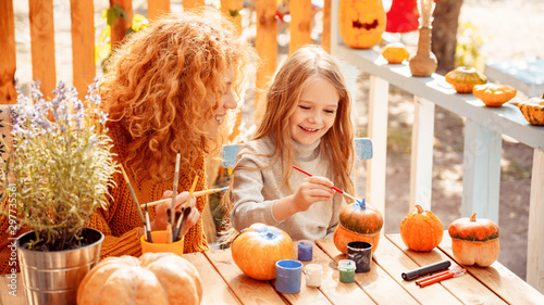 Happy woman drawing on pumpkin with her little daughter photo