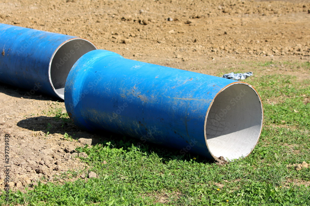 Light blue large diameter construction pipes left on construction site surrounded with grass and dry soil on warm sunny summer day