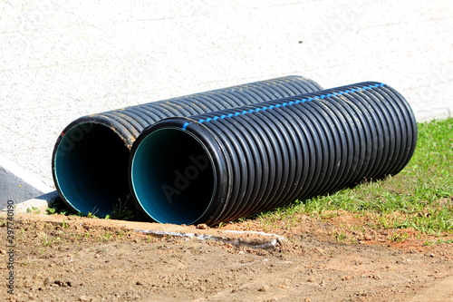 Wallpaper Mural Two black large diameter construction pipes left on construction site surrounded with grass and stone tiles on warm sunny summer day Torontodigital.ca