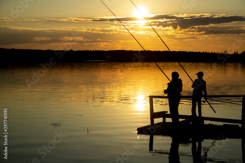 Two silhouettes of fishermen on the lake during sunset .