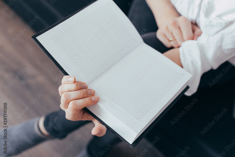 Beautiful female hands hold an open book or magazine in the room Beautiful female hands hold an open book or magazine in the room