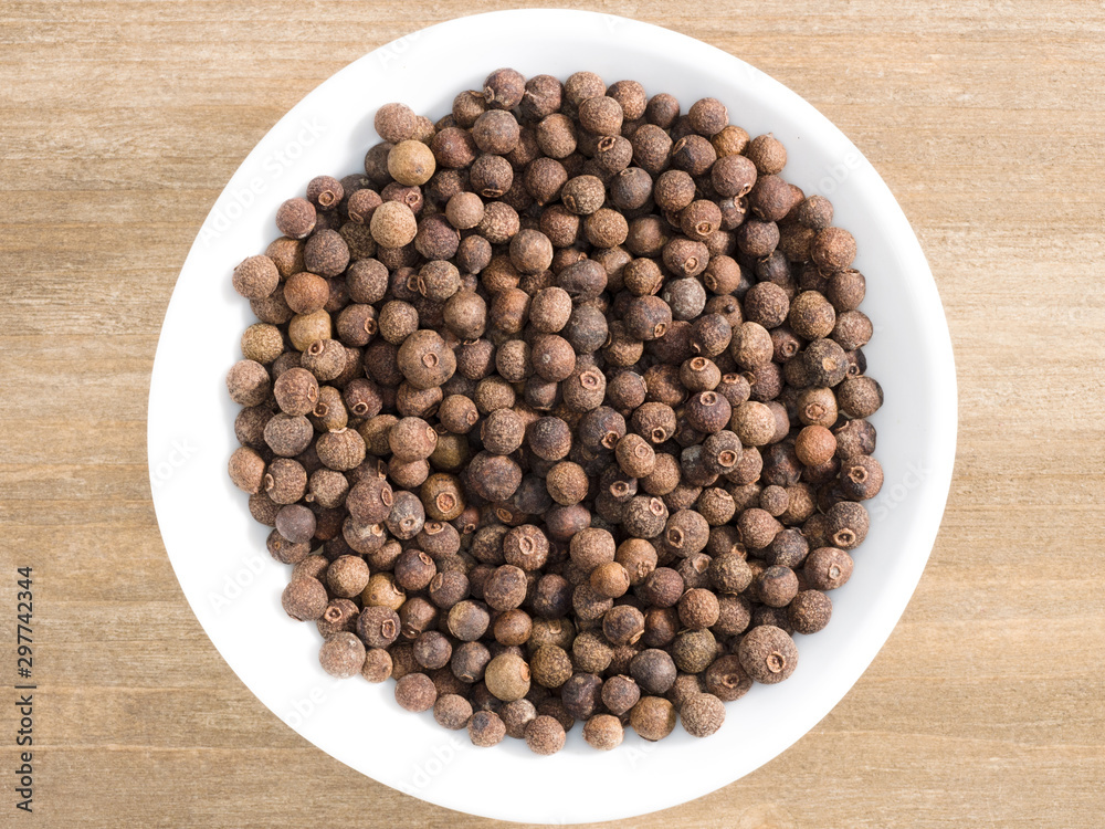 Allspice in white bowl on a brown wooden background. Indian cuisine, ayurveda, naturopathy, modern apothecary concept Allspice in white bowl on a brown wooden background. Indian cuisine, ayurveda, naturopathy, modern apothecary concept