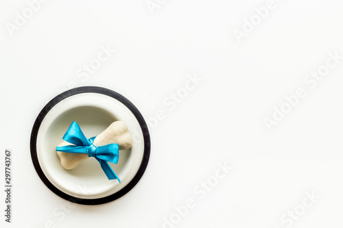 Dog's birthday concept. Chewing bones with bow in bowl on white background top view copy space