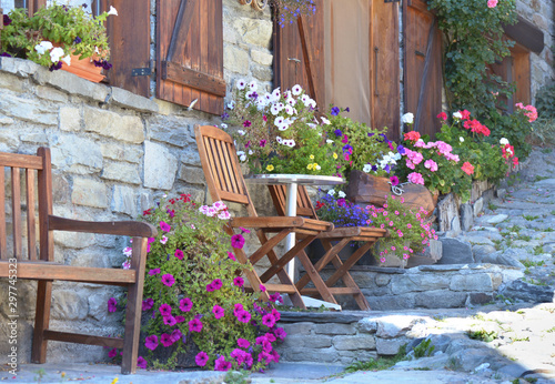 colorful flowers potted and chairs in front of the facade of an alpine house ...