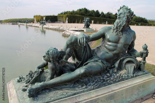 pond and statue in the gardens of the castle of versailles (france)