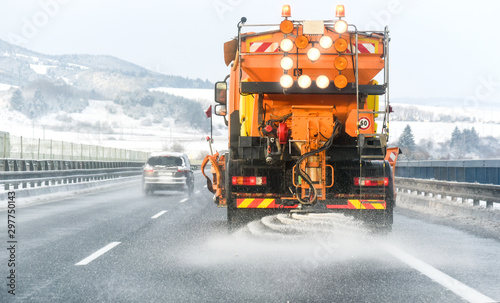 Snow plow on highway salting road. Orange truck deicing street. Maintenance winter vehicle. photo