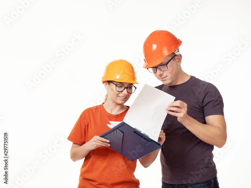 Emotional, young - a man with a woman foreman in yellow helmets with glasses and a folder in his hands on a white background