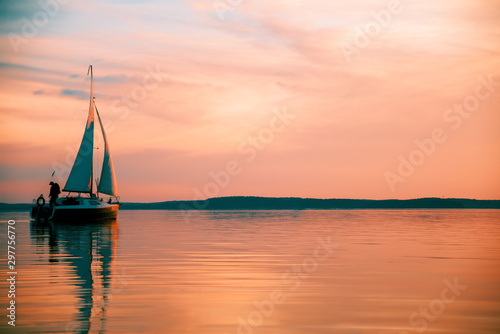 Sailing boat floats on the lake at sunset.