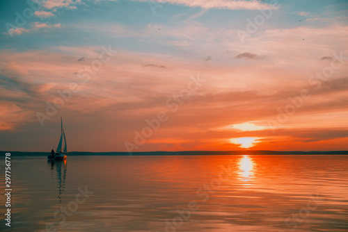 Sailing boat floats on the lake at sunset.