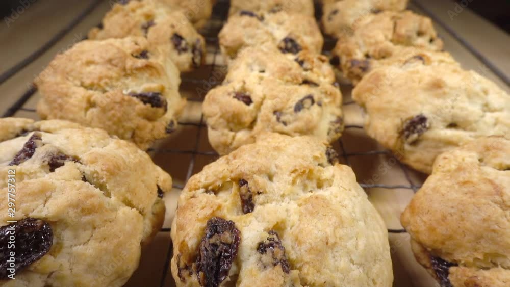 Slow motion close POV reverse dolly shot of traditional, hot, freshly baked, rock cakes / rock buns (small cake with sultanas, with an outer rough surface and soft in the middle) on a cooling grid. Slow motion close POV reverse dolly shot of traditional, hot, freshly baked, rock cakes / rock buns (small cake with sultanas, with an outer rough surface and soft in the middle) on a cooling grid.