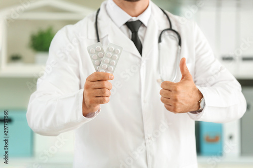 Male doctor with pills showing thumb-up in clinic