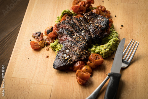 Rinder Hüftsteak auf Holzbrett mit Avocado Püree, geschmolzenen Tomaten, Salz und Steakpfeffer auf Holz Hintergrund dunkel photo