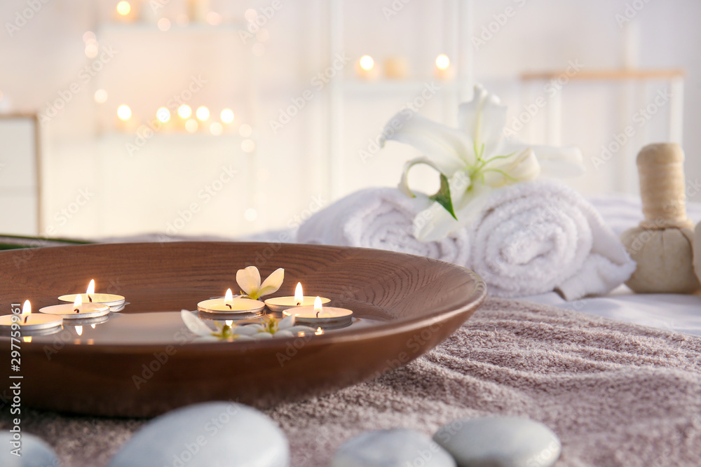 Plate with water and candles on towel in beauty center