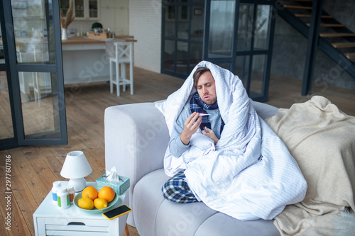 Photography Sick man covered in bedcover sitting on sofa feeling terribly bad