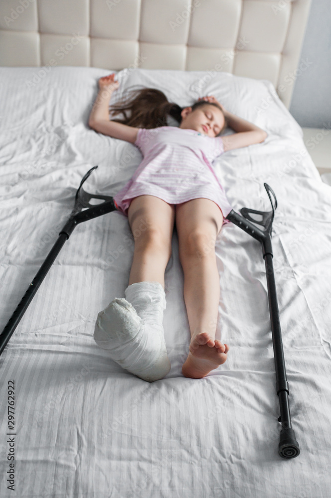 Girl child with a broken leg in a cast lies on a bed with crutches Stock 写真 Adobe Stock