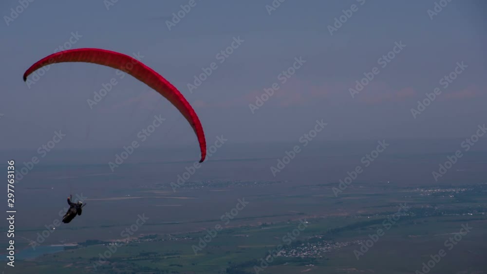 Paragliders Floating in the Air. The sportsman soars in the blue sky on a paraglider on a background of a small town