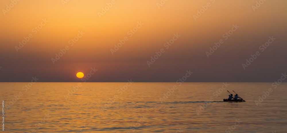 Tandem kayak crossing the sea sailing during sunrise.