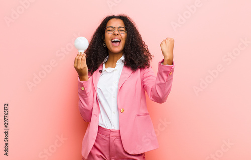 young black pretty woman with a light bulb having an idea against pink wall background