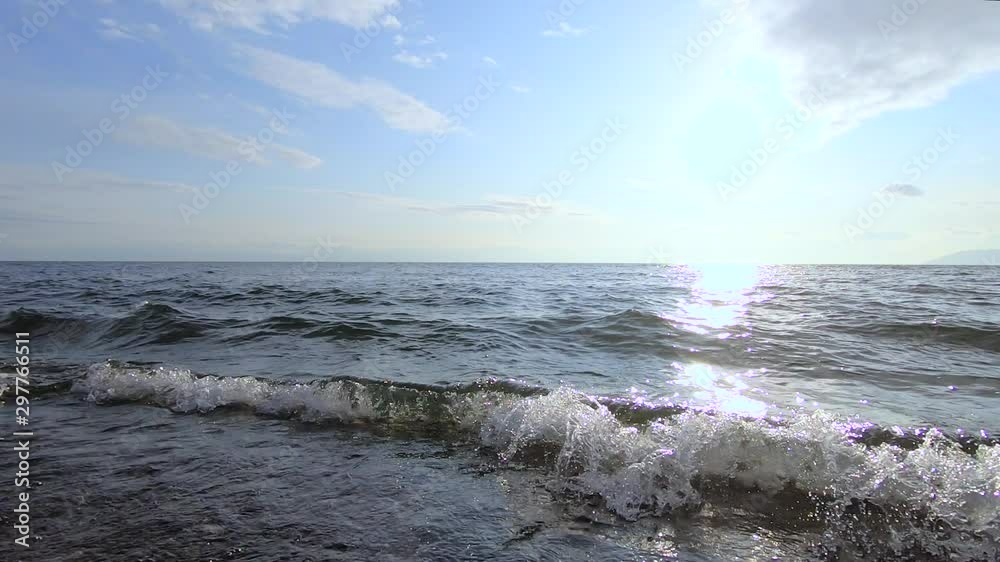 evening white sun against a blue sky, glare from the sun remain on the water, waves beat against the shore evening white sun against a blue sky, glare from the sun remain on the water, waves beat against the shore