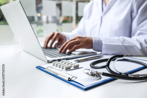 Doctor working with laptop in hospital and medical stethoscope, medicine on clipboard on desk
