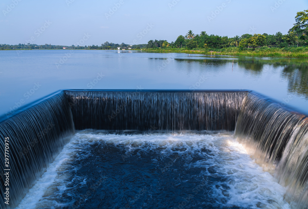 Outdoor and shade of small dam with water flowing rapids. Seen as lines and patterns with foam. The natural swamps abundant and surrounded by forests in the countryside of Thailand.