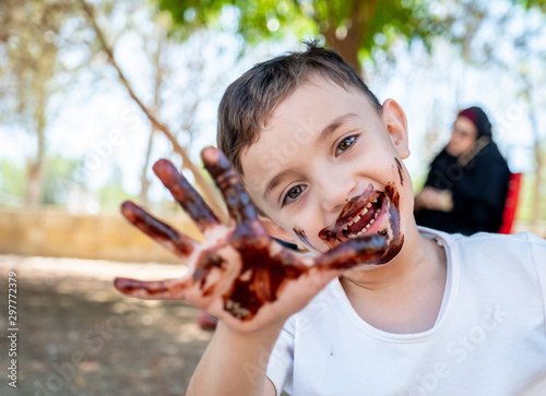 Happy little boy enjoying getting his hands covered with chocolate