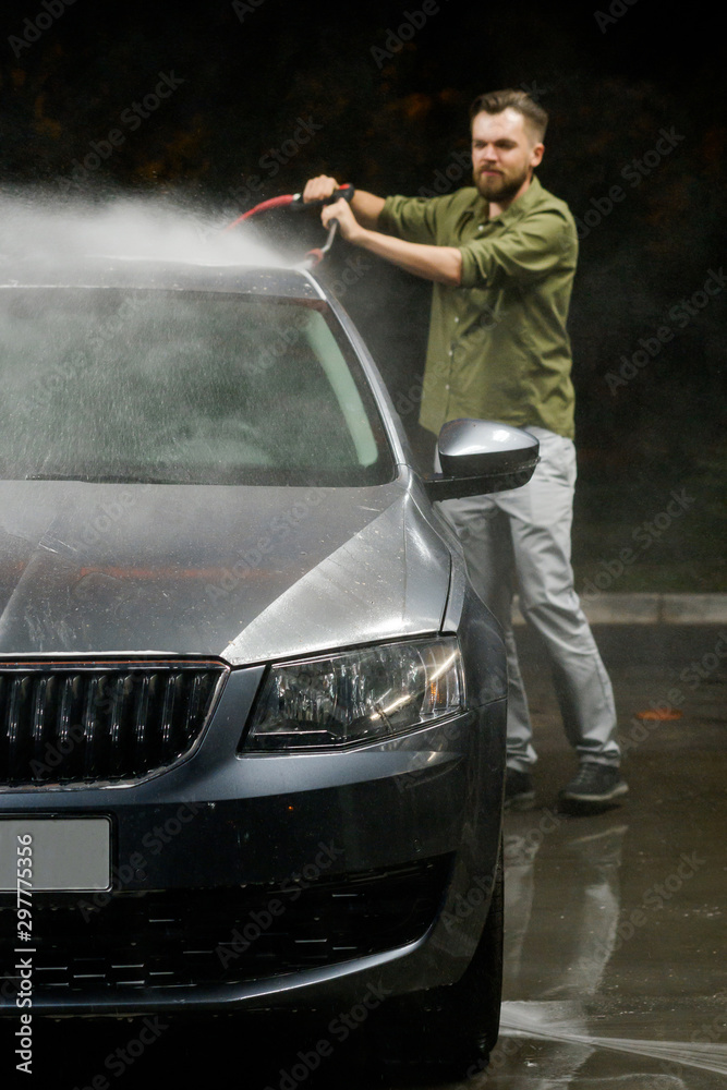 Young man washing his car in car wash. Cleaning Car Using High Pressure