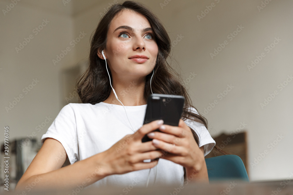 Woman indoors at home using mobile phone and earphones. Woman indoors at home using mobile phone and earphones.