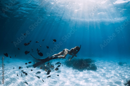 Young woman free diver in bikini glides over sandy sea with fishes. Freediving at Hawaii. photo