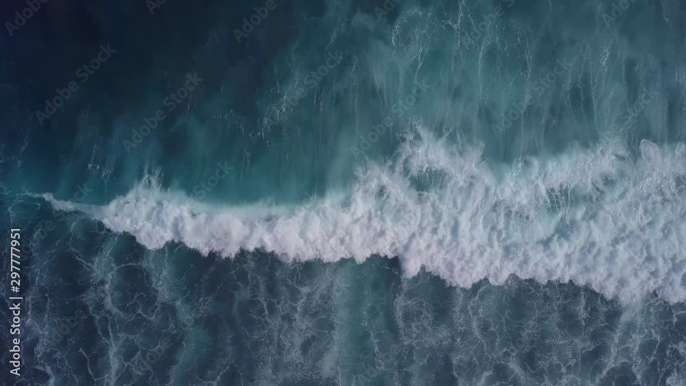 Top down aerial view of giant blue ocean waves breaking, crashing and foaming. Zooming closer