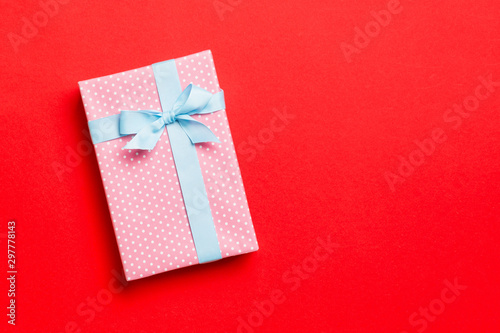 wrapped Christmas or other holiday handmade present in paper with blue ribbon on red background. Present box, decoration of gift on colored table, top view with copy space © sosiukin