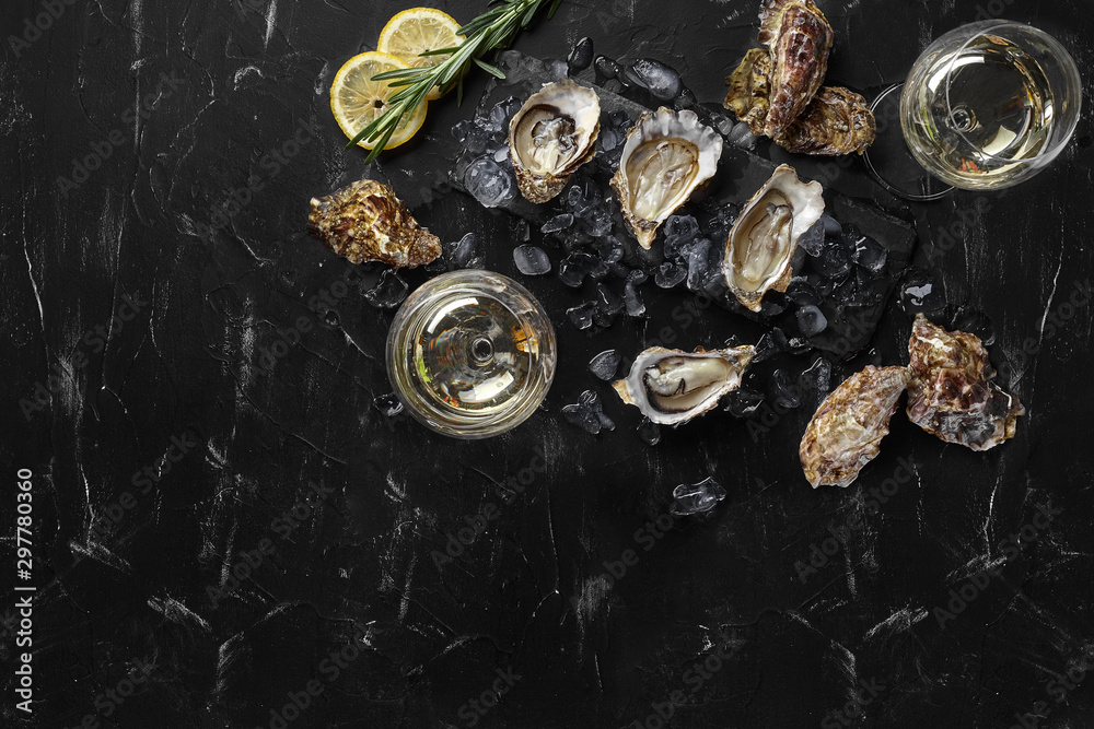Fresh opened oysters, ice, lemon on a rectangle slate and champagne are on a black stone textured background. Top view with copy space. Close-up. Fresh opened oysters, ice, lemon on a rectangle slate and champagne are on a black stone textured background. Top view with copy space. Close-up.