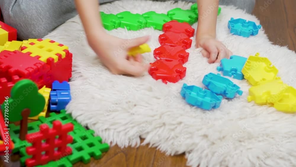 Happy child playing with colored blocks and designer puzzles on white Mat. The kid makes a figure on the carpet. A child and many toys. Camera slide Happy child playing with colored blocks and designer puzzles on white Mat. The kid makes a figure on the carpet. A child and many toys. Camera slide