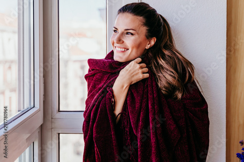 beautiful woman at home by the window, covered with a blanket. lifestyle indoors, autumn season