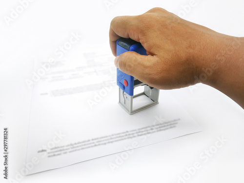 A male hand holding a self-inking, rubber company logo stamp. A paperwork. Office accessories.