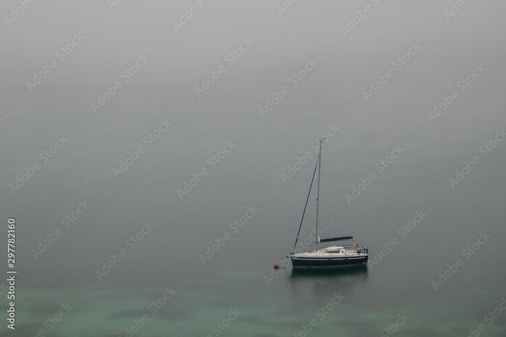 Sailboat sitting on a foggy lake in the morning.