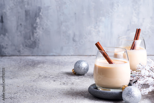 Winter spicy hot drink eggnog in a glasses with cinamon in stone plate, ice frost branches on light stone table photo