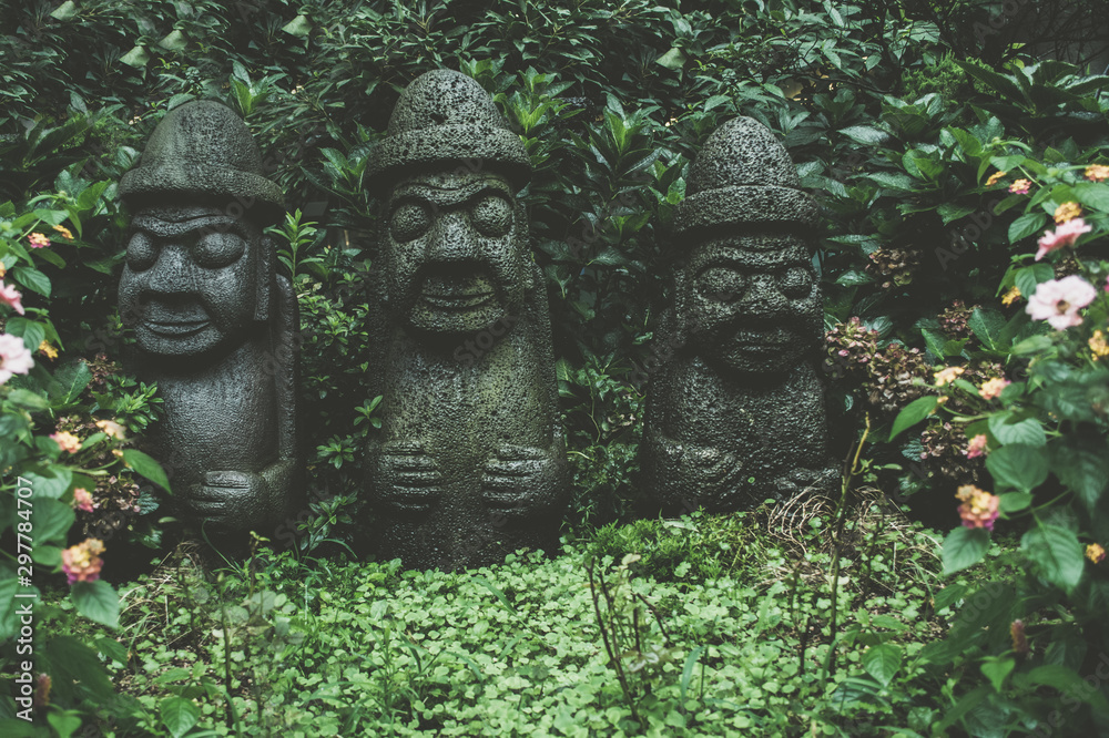 sculptures of Dol Hareubangs on rainy day with green plants sculptures of Dol Hareubangs on rainy day with green plants