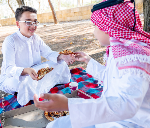 Happy arabic boys enjoying pizza together at the park photo