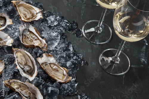 Fresh opened oysters in ice and champagne are on a black stone textured background. Top view. Close-up shot.