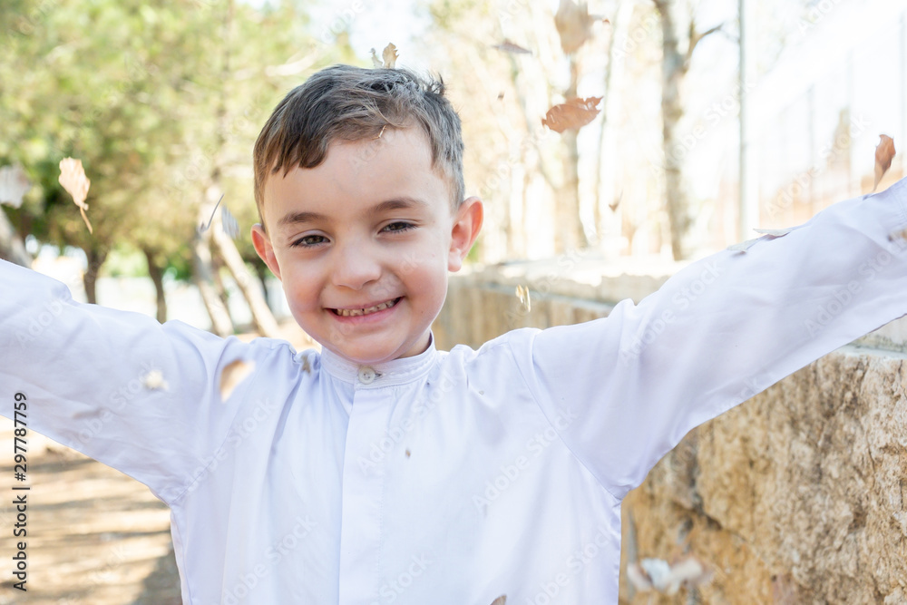 Happy arabic boy enjoying playing with dried leaves outside in th park Happy arabic boy enjoying playing with dried leaves outside in th park