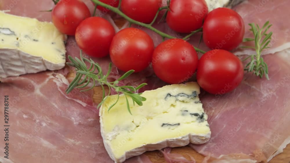 Sliced jamon, cherry tomatoes, pieces of blue cheese and a sprig of lavender laid out on a wooden board, background Sliced jamon, cherry tomatoes, pieces of blue cheese and a sprig of lavender laid out on a wooden board, background